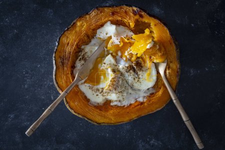 Photo for Half a baked pumpkin along with fried eggs on a dark background, top view, close up - Royalty Free Image