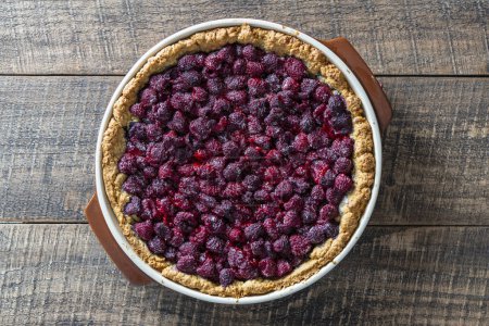 Photo for Raspberry pie in a ceramic dish on wooden background, close up, top view - Royalty Free Image