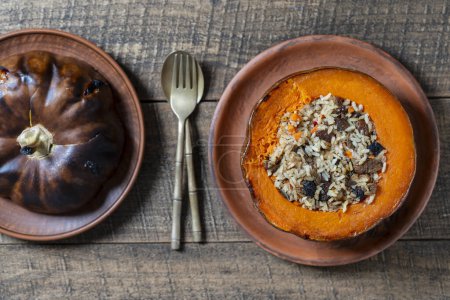 Téléchargez les photos : Grande citrouille cuite avec un gros plan de remplissage. Citrouille orange rôtie farcie, cuite au four, remplie d'un savoureux mélange de riz, raisins secs et épices sur une table en bois, vue sur le dessus - en image libre de droit