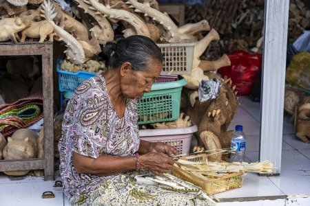 Téléchargez les photos : Ubud, Bali, Indonésie - 03 avril 2019 : Une femme âgée indonésienne fait des souvenirs pour les touristes à un marché de rue dans le centre d'Ubud, île de Bali, Indonésie - en image libre de droit