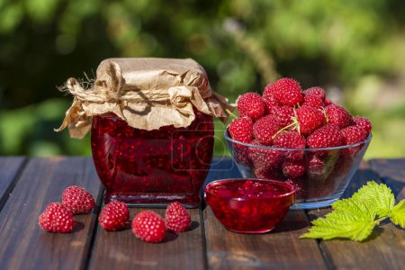 Photo for Red raspberry jam and fresh raspberry on a rustic wooden table outdoors near garden. Rustic style, close up - Royalty Free Image