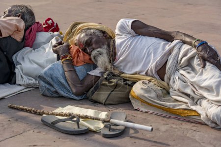 Foto de Haridwar, India - 10 de noviembre de 2018: Un indigente no identificado duerme en la acera cerca del río Ganges en la ciudad santa de Haridwar, India. Pobres indios acuden a Haridwar por caridad - Imagen libre de derechos