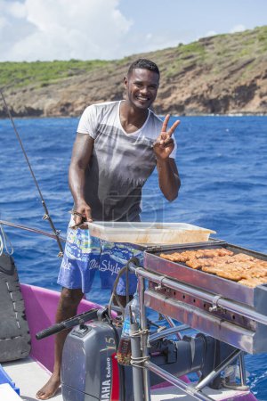 Foto de Port Louis, Isla Mauricio - 18 de marzo de 2017: El chef africano cocina barbacoa a la parrilla en la estufa para servir a los pasajeros de viajes turísticos en barco privado en vacaciones de verano en el océano Índico, Mauricio - Imagen libre de derechos