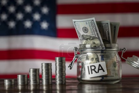 Photo for Money towers and glass jar used for saving US dollar bills and notes for IRA retirement fund on the American flag background, close up. Finance, business, investment and money saving concept - Royalty Free Image