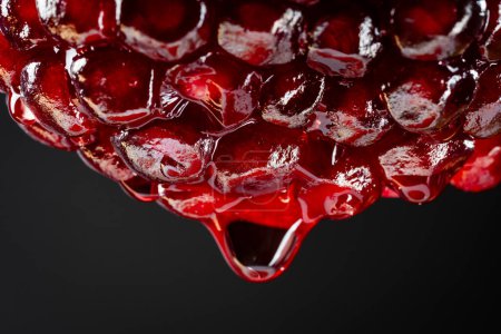 Foto de Zumo de granada roja goteando de la mitad de la fruta sobre fondo negro, macrofotografía. Textura fruta fresca, primer plano - Imagen libre de derechos