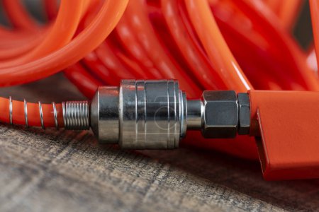 Photo for An orange air hose with an hose coupling on a wooden background, close up. Detail of air compressor hose and pistol - Royalty Free Image