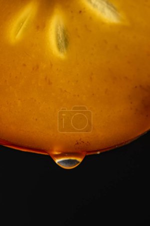 Téléchargez les photos : Tranche de kaki d'orange avec des gouttes de jus sur fond noir, macro photographie. Texture fruits frais, gros plan - en image libre de droit