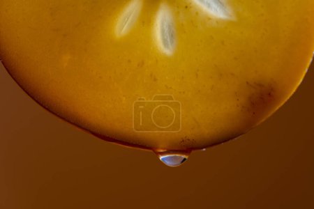 Foto de Rebanada de caqui con gotas de jugo sobre un fondo naranja, macrofotografía. Textura fruta fresca, primer plano - Imagen libre de derechos