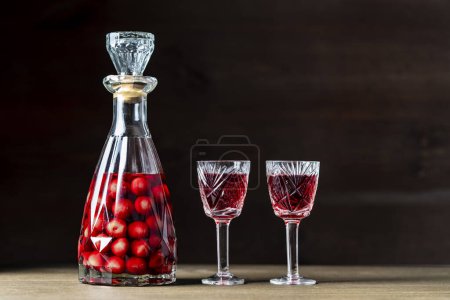 Photo for Homemade cherry brandy in two glasses and in a glass bottle on a wooden background, close up - Royalty Free Image
