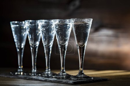 Photo for Selective focus of five shot glasses of cold vodka on wooden table, close up - Royalty Free Image