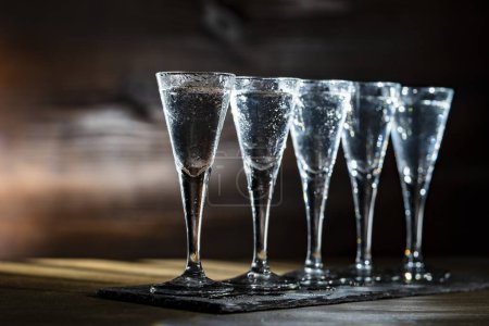 Foto de Enfoque selectivo de cinco vasos de vodka frío en la mesa de madera, de cerca - Imagen libre de derechos