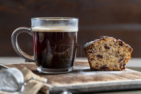 Téléchargez les photos : Délicieux muffin aux cerises rouges, noix et tasse en verre de café noir sur une table en bois, fermer. cupcake frais et café pour le petit déjeuner - en image libre de droit