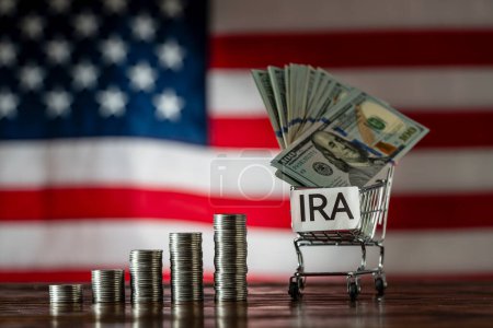 Photo for Money towers and shopping cart used for saving US dollar bills and notes for IRA retirement fund on the American flag background, close up. Finance, business, investment and money saving concept - Royalty Free Image