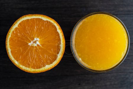 Photo for Half an orange and a glass of freshly squeezed orange juice on a wooden background, close up, top view - Royalty Free Image