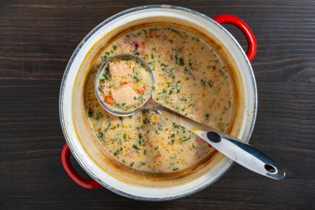 Photo for Leftovers cream fish soup in a saucepan with a ladle on a wooden table, close up, top view - Royalty Free Image