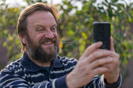 Photo for Happy senior adult man rest in nature get message from old friend. Mature man reading good news on phone screen. Elderly male with mobile cell phone - Royalty Free Image