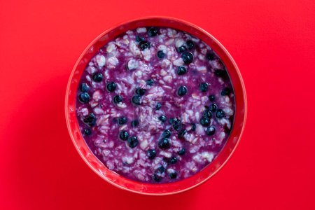 Téléchargez les photos : Bouillie d'avoine aux bleuets mûrs pour un petit déjeuner sain sur fond rouge, gros plan, vue sur le dessus - en image libre de droit