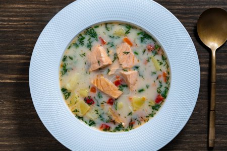 Photo for Fresh creamy salmon fish soup with potatoes, carrots, peppers and onions in a ceramic plate on a wooden table, close up, top view. A delicious dinner consists of fish soup with salmon - Royalty Free Image
