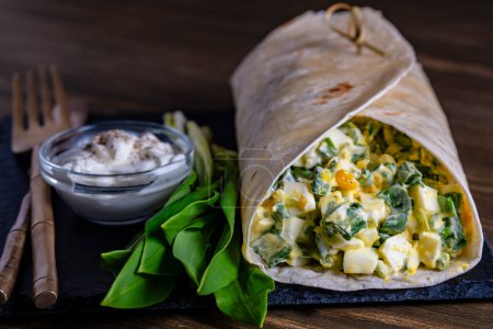 Téléchargez les photos : Burrito maison enveloppé d'œufs durs, de pommes de terre, d'ail vert sauvage et de crème sure pour un petit déjeuner sain dans une assiette, fermez - en image libre de droit