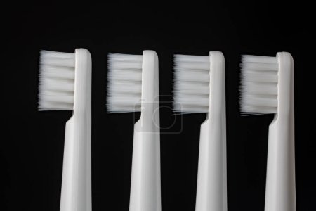Foto de Cuatro cepillos de dientes de plástico blanco sobre un fondo negro, de cerca - Imagen libre de derechos