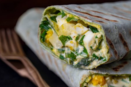 Foto de Burrito casero envuelve con huevos cocidos, patatas, ajo verde silvestre y crema agria para el desayuno saludable, de cerca - Imagen libre de derechos