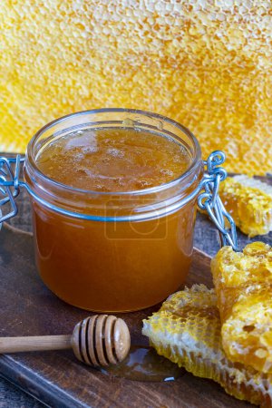 Téléchargez les photos : Un bocal en verre de miel doré épais avec une cuillère en bois et des rayons de miel. Concept d'apiculture, apiculture, rucher. Miel sucré, aliments sains - en image libre de droit