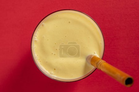 Photo for Banana mango smoothie with a bamboo straw on a red background, close up, top view - Royalty Free Image