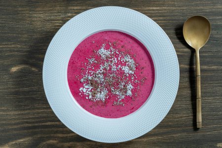 Sweet summer cherry soup in a white plate on a wooden background, close up, top view. Hungarian cold red cherry soup with yogurt or cream, sprinkled with grated chocolate and powdered sugar