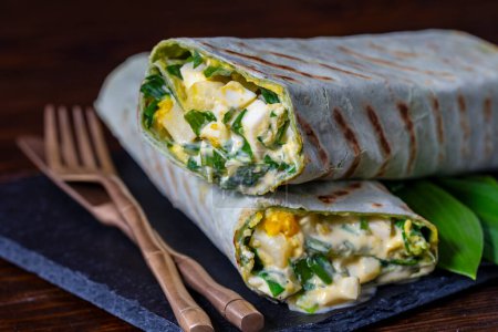 Foto de Burrito casero envuelve con huevos cocidos, patatas, ajo verde silvestre y crema agria para el desayuno saludable, de cerca - Imagen libre de derechos