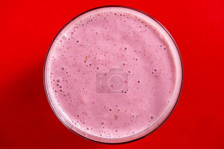 Photo for Raspberry banana smoothie in glass on a red background, close up, top view - Royalty Free Image