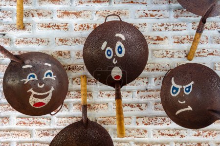 Photo for Old frying pans with painted faces, hang on a brick wall, close up - Royalty Free Image