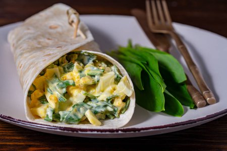 Photo for Homemade burrito wraps with boiled eggs, potato, green wild garlic and sour cream for healthy breakfast on plate, close up - Royalty Free Image