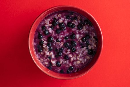 Photo for Oatmeal porridge with ripe blueberries for healthy breakfast on red background, close up, top view - Royalty Free Image