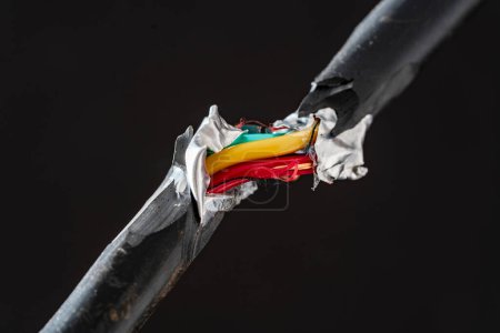 Foto de Un primer plano de un cable eléctrico roto con cables rojos y amarillos eléctricos entrelazados. Cable eléctrico de alimentación dañado sobre fondo negro - Imagen libre de derechos