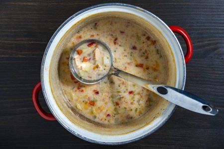 Photo for Leftovers cream fish soup in a saucepan with a ladle on a wooden table, close up, top view - Royalty Free Image