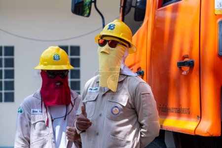 Foto de Koh Phangan, Tailandia - 26 de enero de 2022: Dos electricistas tailandeses con máscaras de protección solar están junto a un vehículo técnico en la isla Koh Phangan, Tailandia - Imagen libre de derechos