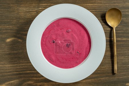 Süße Sommerkirschsuppe in einem weißen Teller auf hölzernem Hintergrund, Nahaufnahme, Draufsicht. Ungarische kalte rote Kirschsuppe mit Joghurt oder Sahne