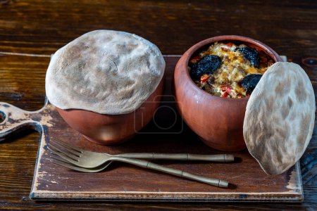Photo for Two clay pots with stewed vegetables on a wooden table, close up. Stewing food in earthenware is considered healthy - Royalty Free Image