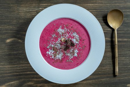 Sweet summer cherry soup in a white plate on a wooden background, close up, top view. Hungarian cold red cherry soup with yogurt or cream, sprinkled with grated chocolate, powdered sugar and hazelnuts