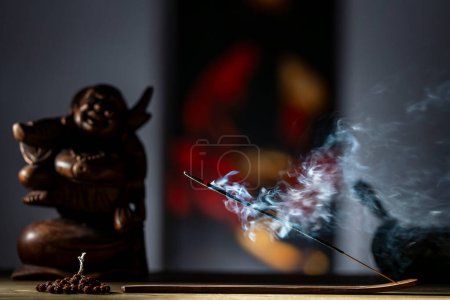Photo for Asian incense stick in stick holder burning with smoke on dark background, close up. Meditation, yoga, self development and sound therapy concept - Royalty Free Image