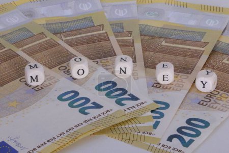 Stacks of 200 euro bills lie fanned out on the table and on them are wooden cubes with letters that spell out the name money