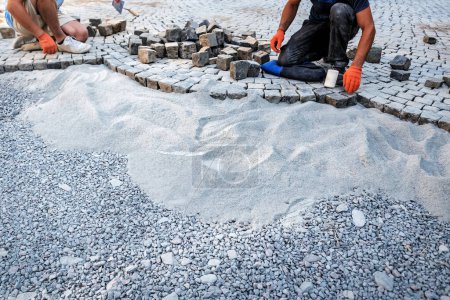 Foto de Colocación de cubos de granito pavimento de piedra en la calle de la ciudad con el trabajador de la construcción de carreteras. Tema industrial - Imagen libre de derechos