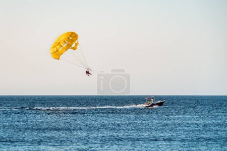 Photo for Parasailing by boat water amusement. Flying on a parachute behind a boat on a summer holiday. Vacation theme - Royalty Free Image