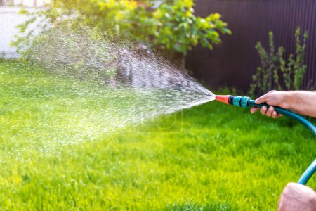 Photo for Gardener's hand holds a hose with a sprayer and watering green grass - Royalty Free Image