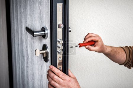 Téléchargez les photos : Professionnel bricoleur réparer la serrure de porte dans la porte d'entrée en métal, Homme serrure de fixation avec tournevis - en image libre de droit