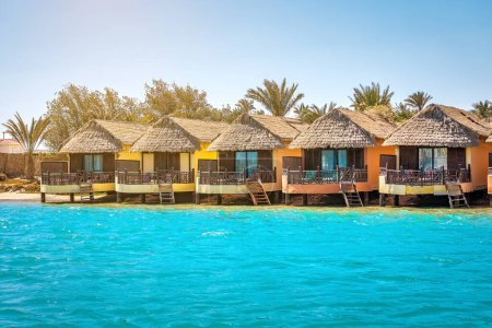 Téléchargez les photos : Rangée de bungalows en bois avec toit en paille dans l'eau de mer sous le soleil. Thème vacances - en image libre de droit