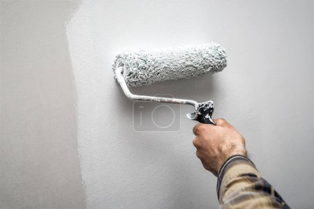 Téléchargez les photos : Main tenant un rouleau de peinture tout en peignant un mur de la maison. Thème industriel - en image libre de droit