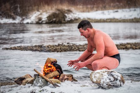 Photo for A man walrus warms himself by a fire after swimming in a winter river. Healthy lifestyle - Royalty Free Image