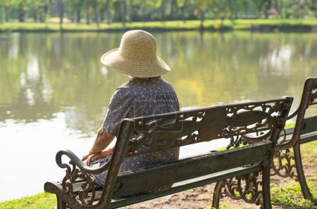 Photo for Asian elderly woman depressed and sad sitting back on bench in autumn park. - Royalty Free Image