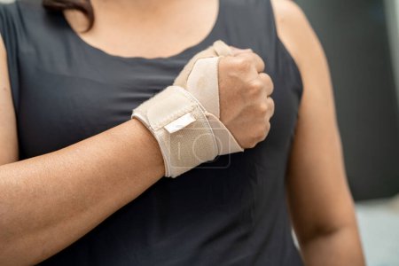 Foto de Mujer asiática usa vendaje elástico para tratar el síndrome de De Quervain en la mano y el dedo en el consultorio. - Imagen libre de derechos